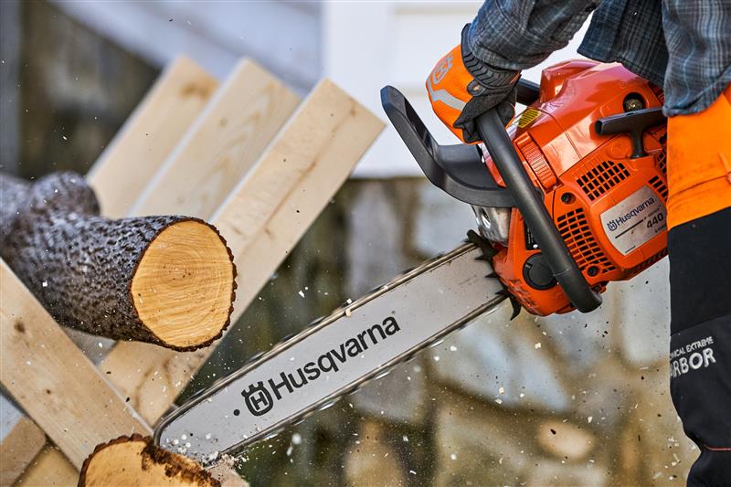 Mann der mit einer Husqvarna Motorsäge einen Baum schneidet (Nahaufnahme der Motorsäge)